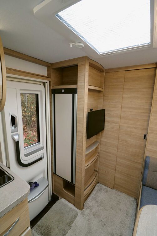 Armoire haute multifonction avec espace TV, diverses tablettes et réfrigérateur à l’entrée.