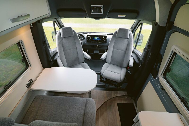 L’élégant intérieur présente un design moderne avec des touches argentées et des trappes blanches, un tissu de coussins gris clair et un revêtement de sol effet bois sombre.